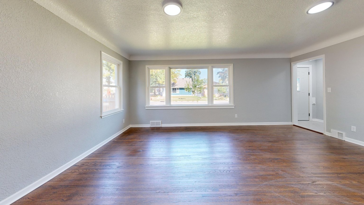 Empty room with hardwood floor, grey walls and a large window, before any staging